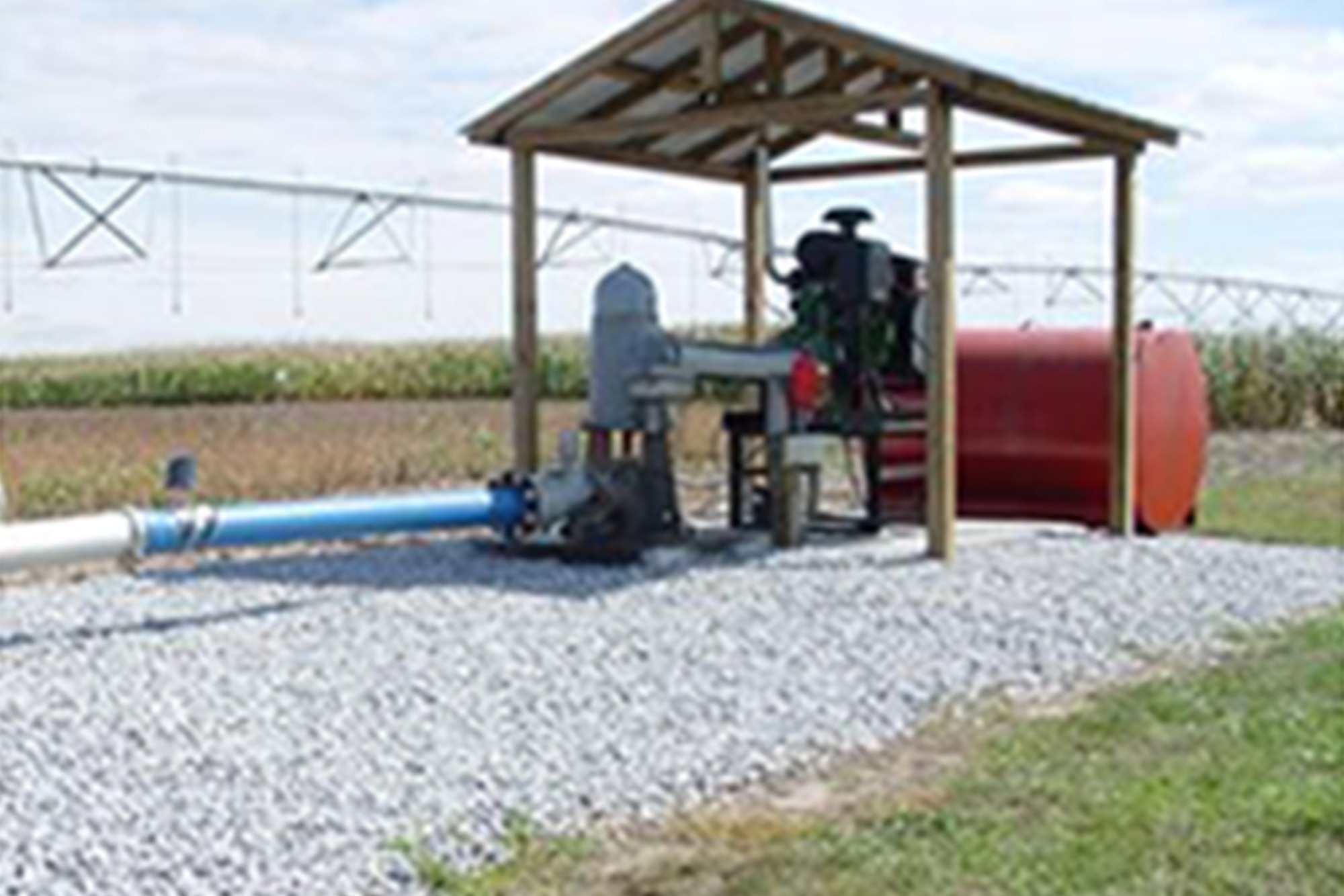 Agricultural irrigation pump with red fuel tank sheltered under a wooden structure in a farm field