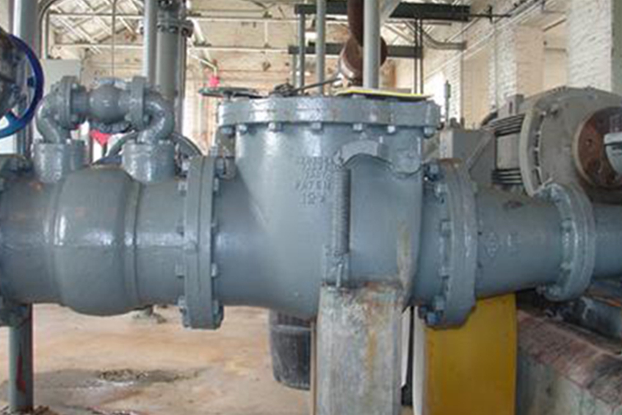 Industrial gray piping system with large valves and gauges inside a factory building