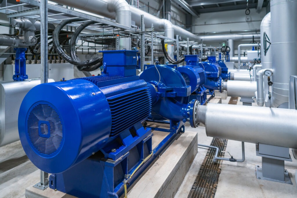 A row of large blue industrial pumps with electric motors connected to silver piping in a modern facility