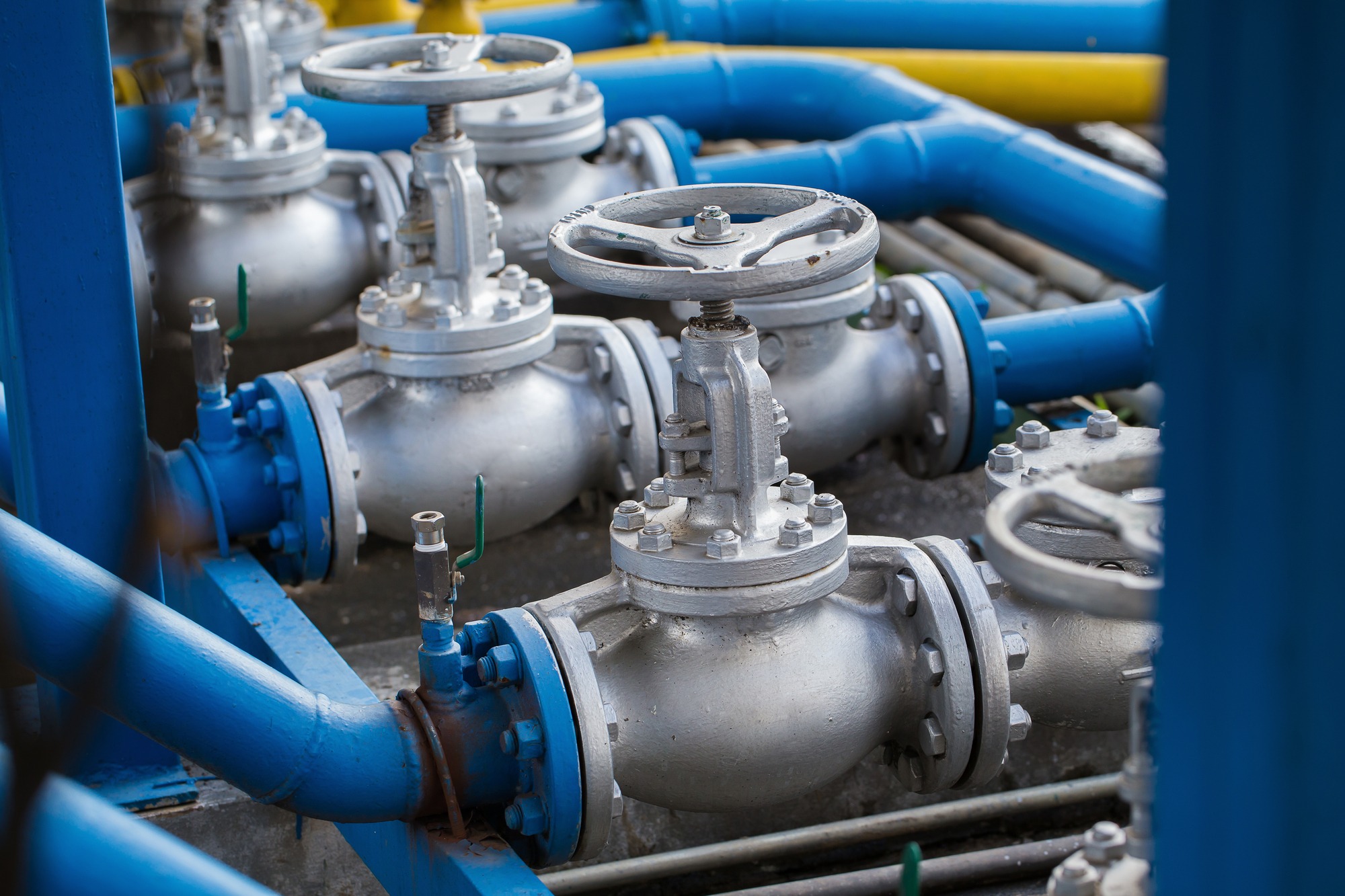 Industrial gate valves with large handwheels and bolted flanges connected to bright blue pipes